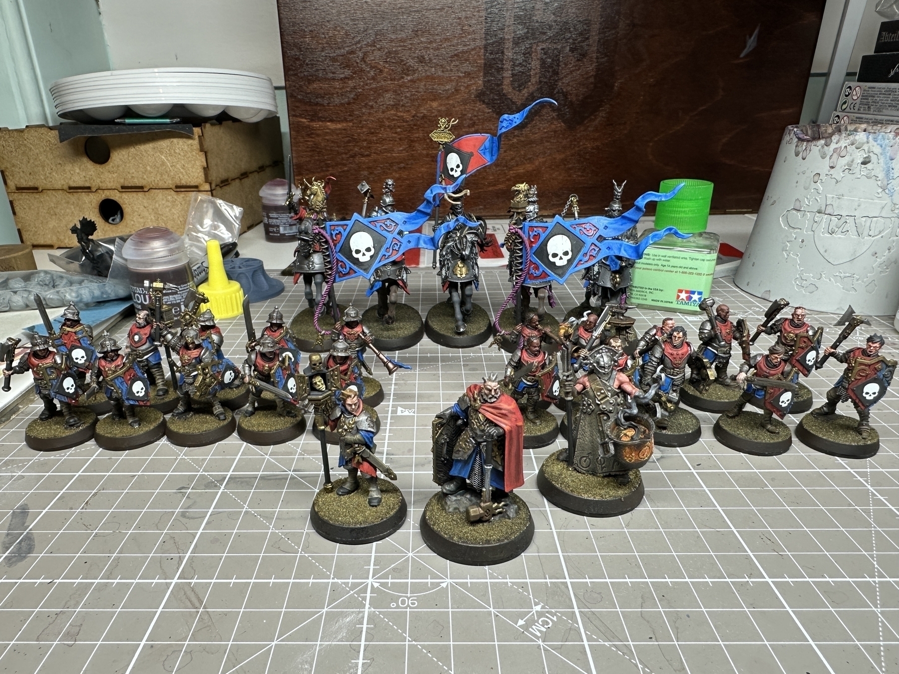 Miniatures from the Cities of Sigmar range, by Games Workshop. They are fully painted and arranged for display. The dominant uniform colours are blue, red, silver, and gold. The army iconography consists of a white skull on a black background
