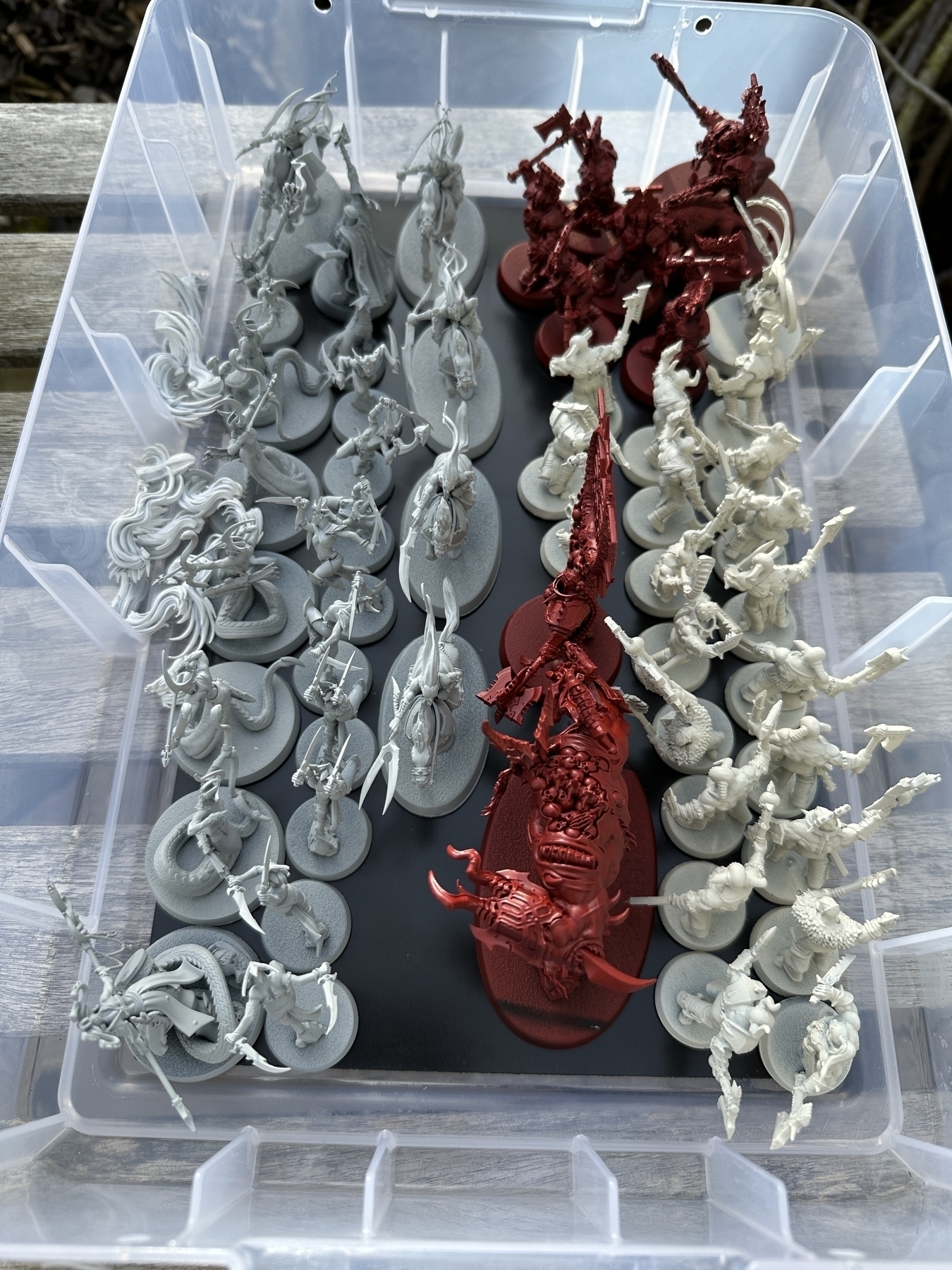 A box of games workshop miniatures that have been sprayed with various colours of primer. There are 23 in light grey, 8 in bright red, and 21 in warm, off-white